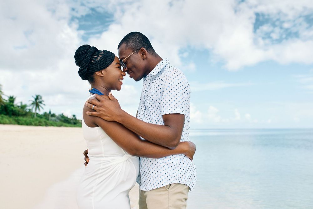 A loving couple shares an intimate moment on a scenic beach with palm trees in the background.