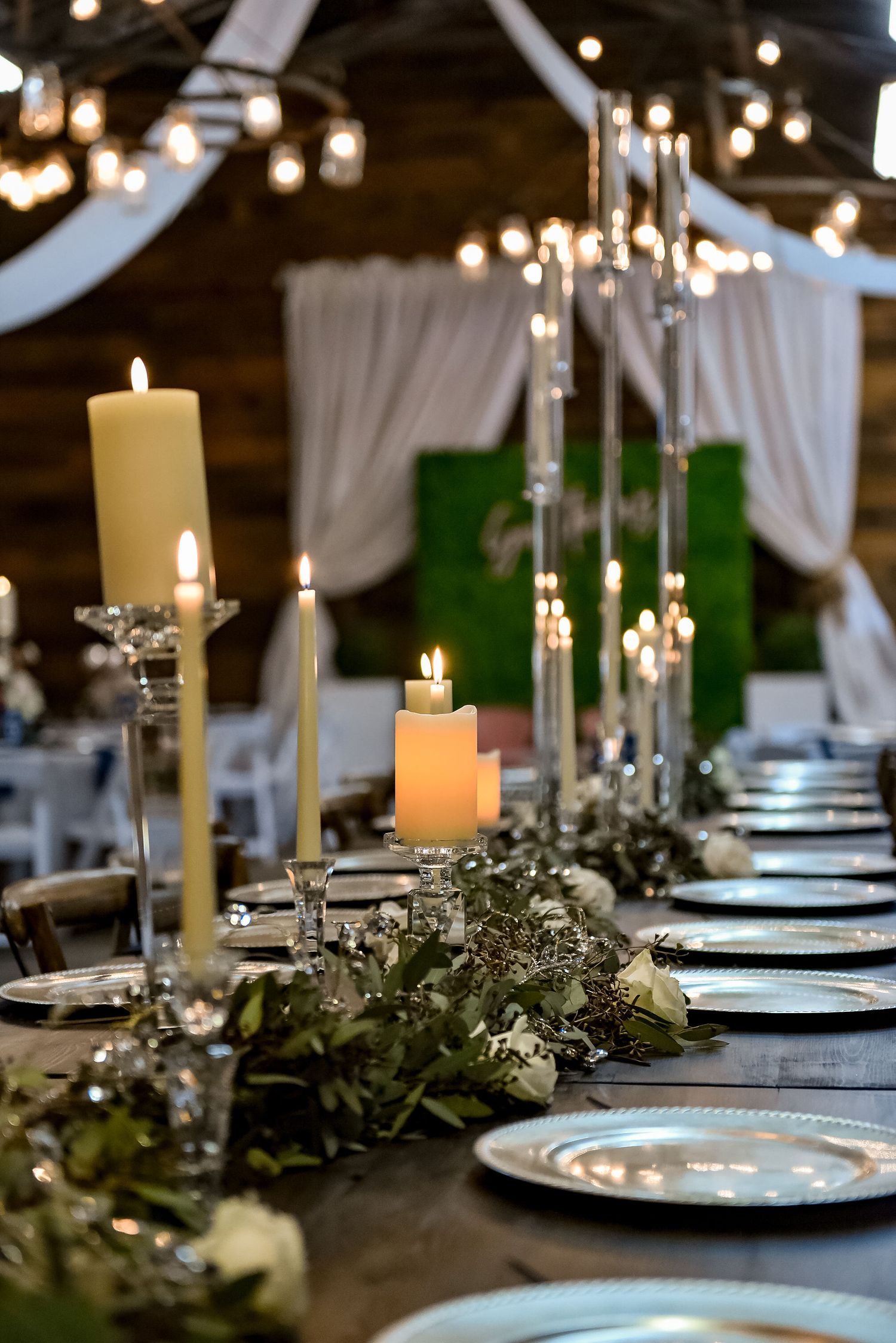 An elegant wedding table setting with lit candles, greenery, and silver charger plates.