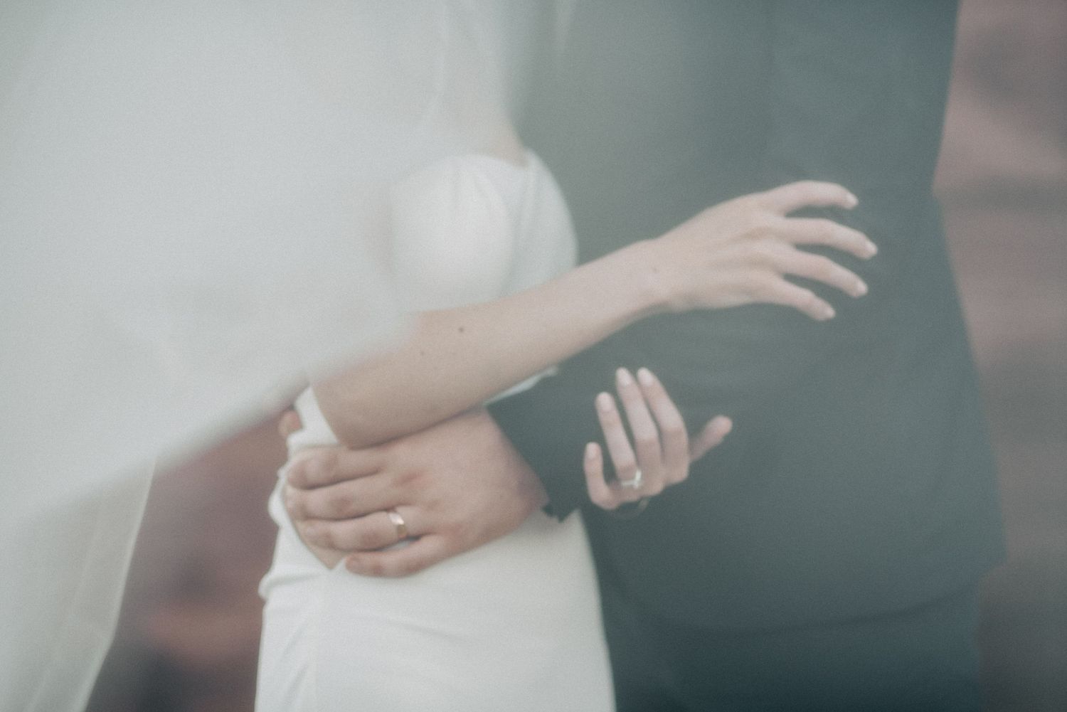 Soft focus detail of white wedding dress and embracing arms.