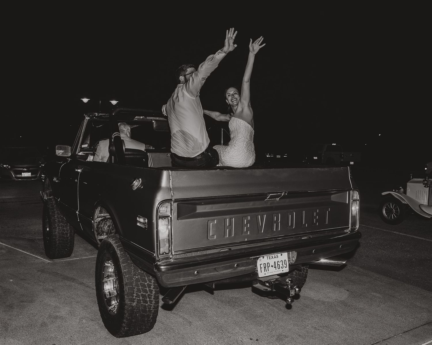 Black and white photo of celebratory poses in the back of a vintage Chevrolet truck.