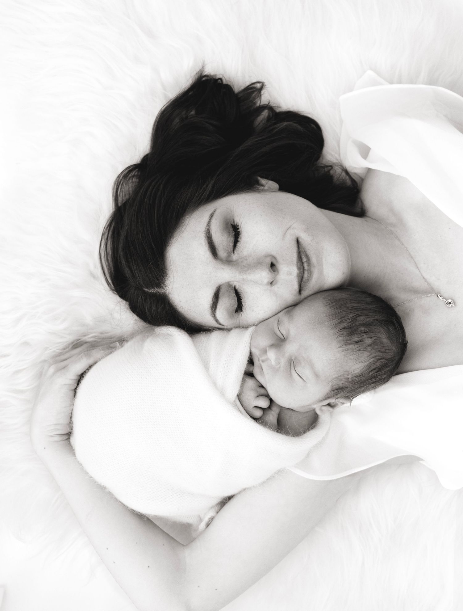 Mother and newborn snuggle cheek to check on a soft white sheepskin rug