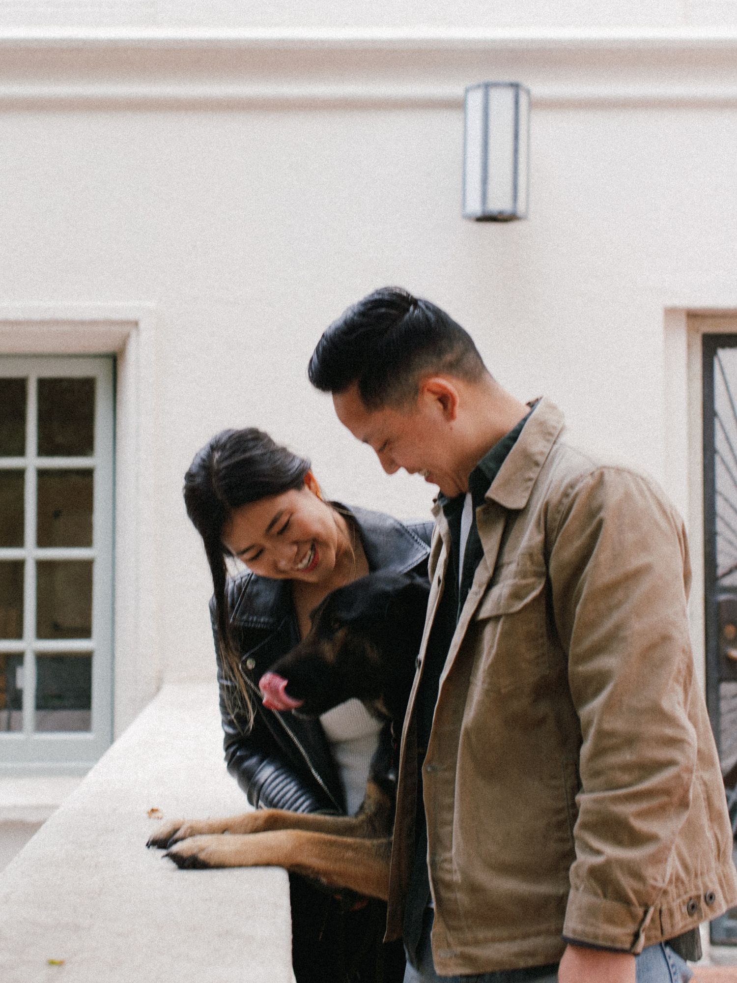 Casual couple sharing a lighthearted moment outside a white building with windows.