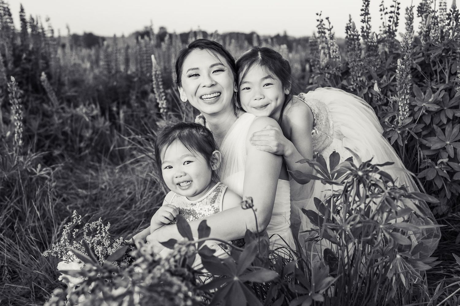 Black and white photo of mother with her daughters in a wildflower field.