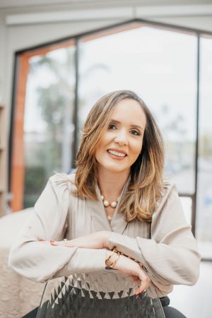 Professional portrait in beige blouse leaning on office chair.