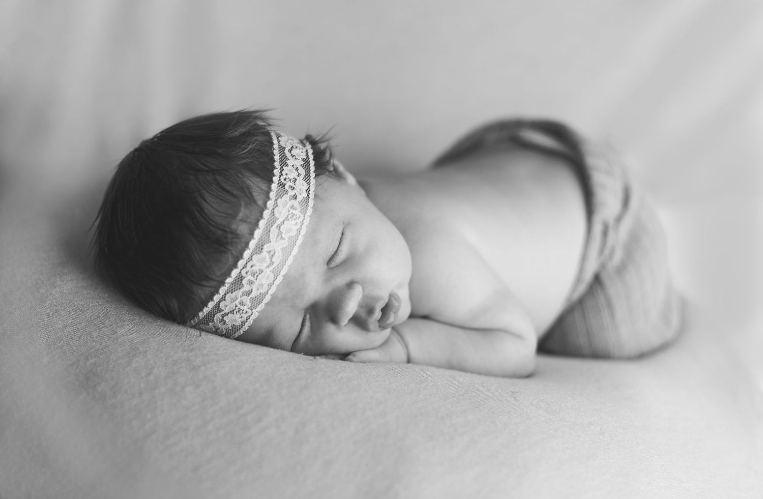 Peaceful sleeping newborn wearing delicate headband in black and white portrait.