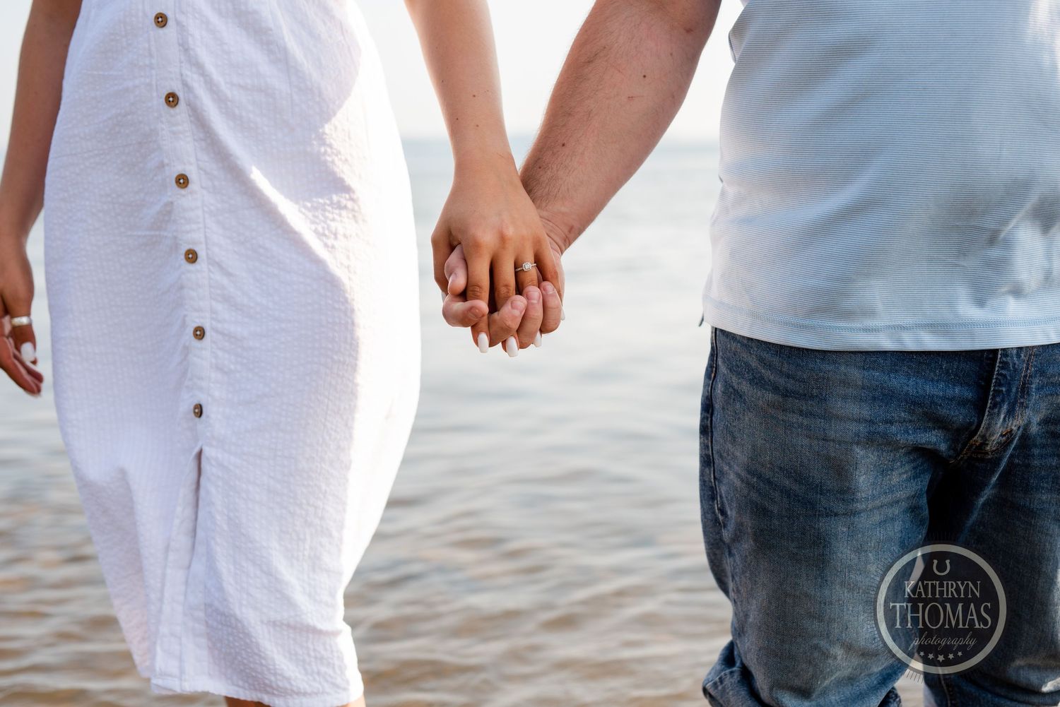 Two people holding hands while walking along the water's edge.