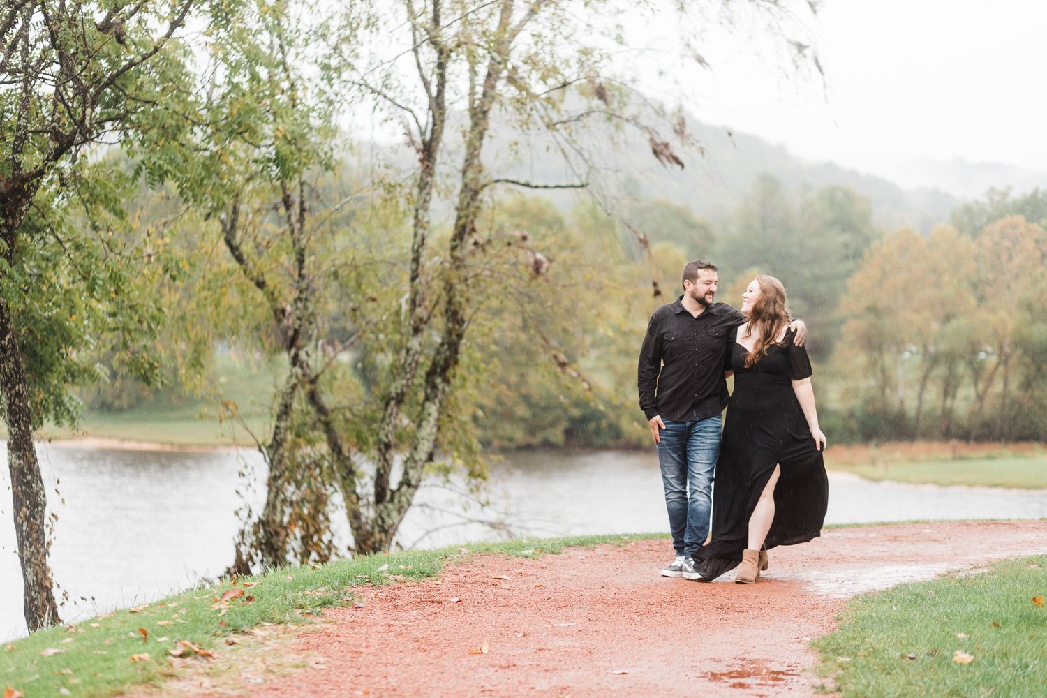 Couple walking along lakeside path surrounded by autumn trees and water views.
