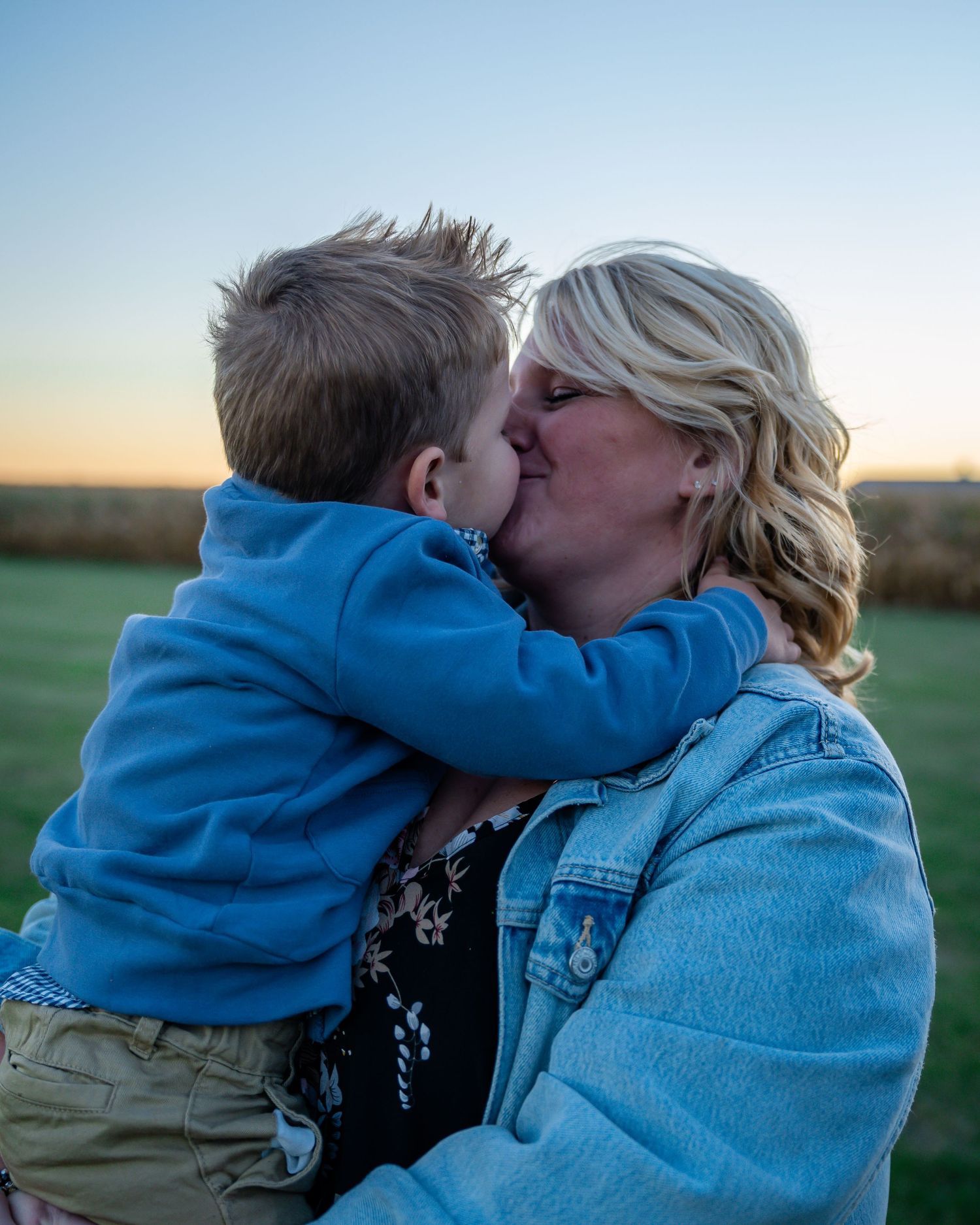 A tender moment shared at sunset in a field with a blue sky backdrop.