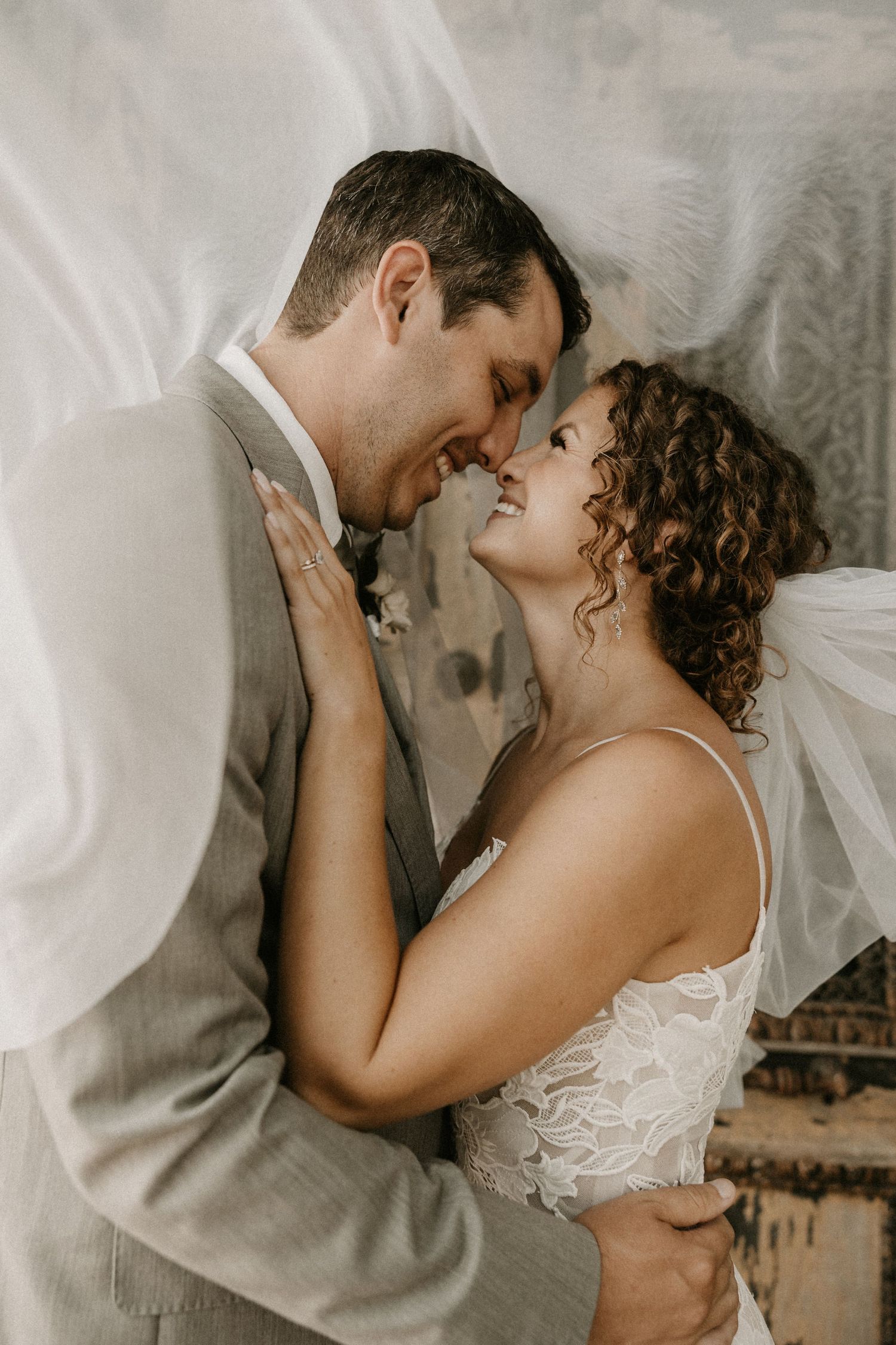 Romantic wedding portrait with couple sharing tender moment against lace backdrop.