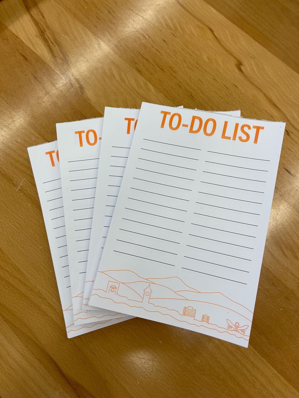 Four to-do list notepads with minimalist mountain design on wooden surface.