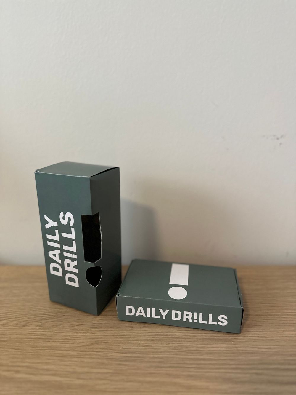 Two dark green boxes with 'Daily Drills' branding displayed on wooden surface.