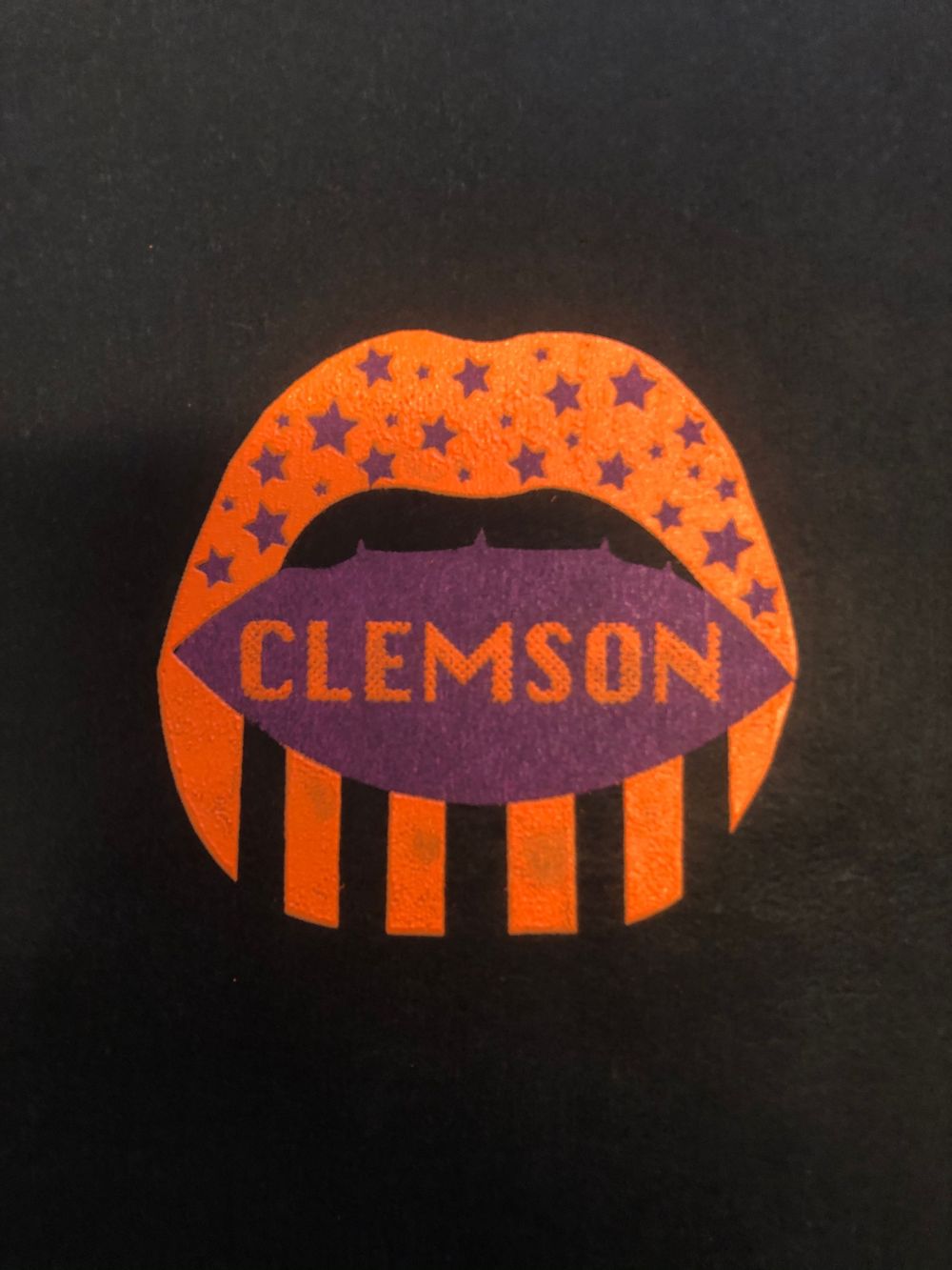 Orange and purple lip-shaped design featuring Clemson text and stars on black background.