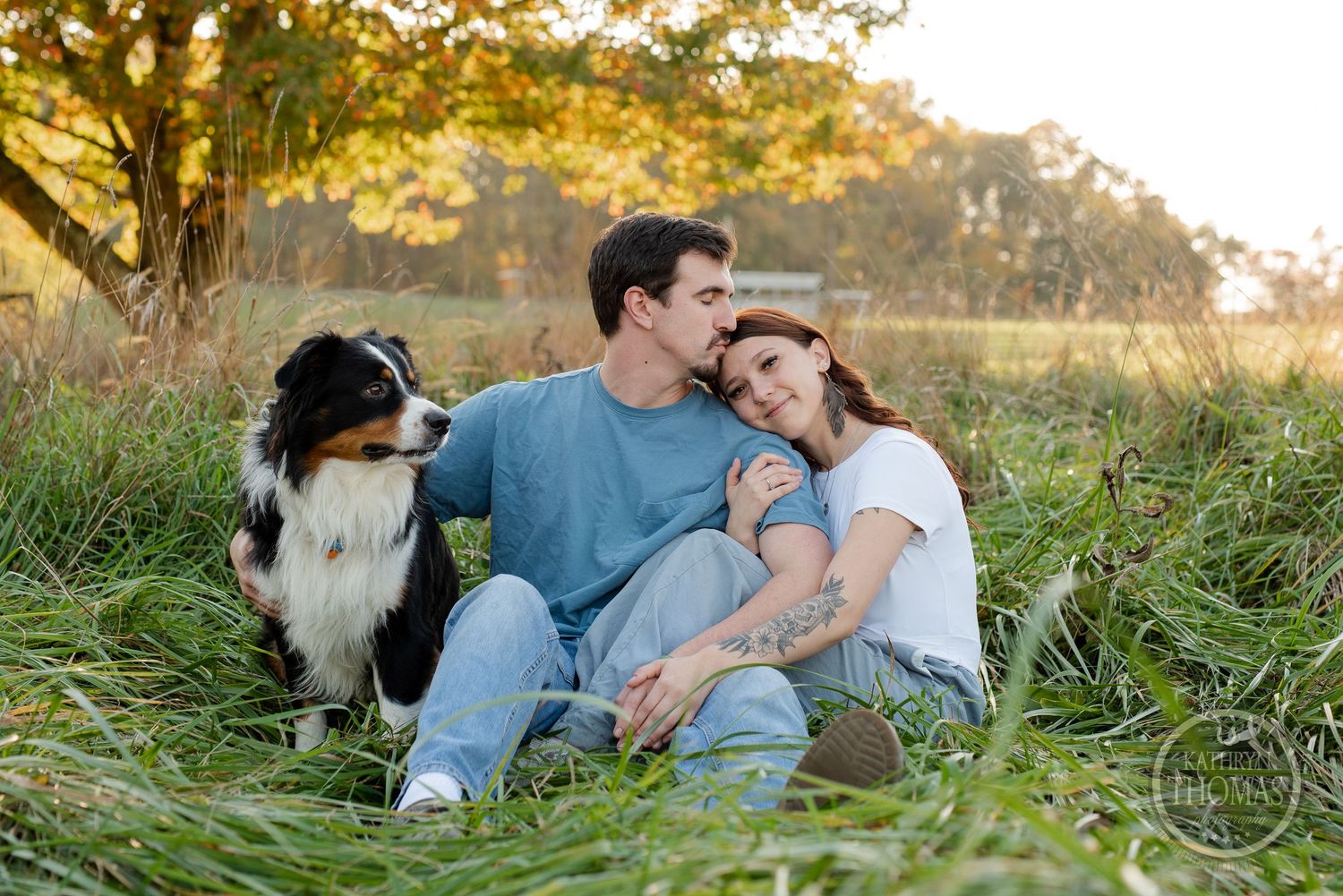 A couple lounges in tall grass with their black and white Border Collie during sunset.