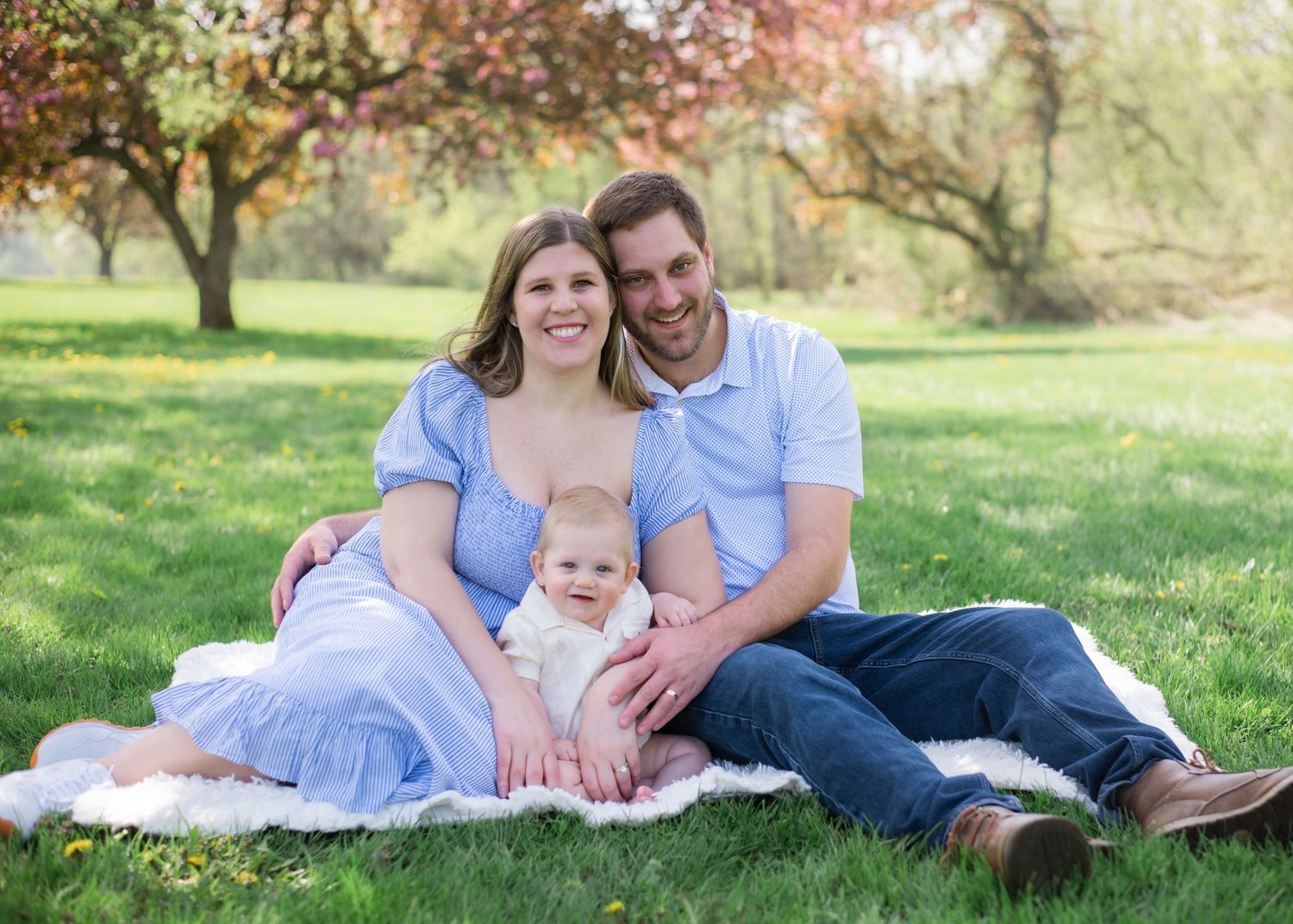Family lounging on blanket in sunny spring garden with blooming trees in background.