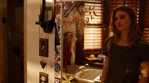 Interior scene shows figure standing near decorative wall with venetian blinds in background.