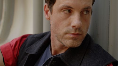 Person in black jacket and red shirt looking intensely at camera.