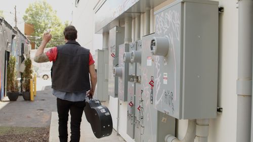 Person carrying bag walking past electrical meters on exterior wall.
