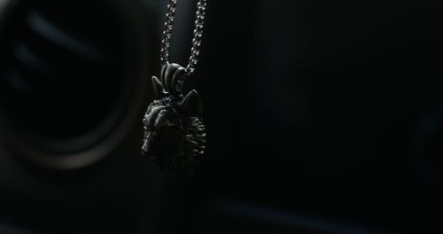 Dark artistic shot of pendant necklace hanging against black background.