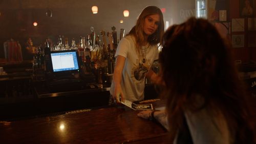 Bartender serving customers at a dimly lit bar counter with electronic display.