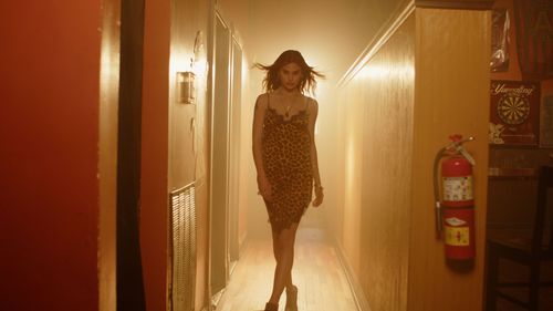 Person walking down a hallway in a dress silhouetted by warm lighting.