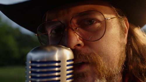 Close-up of musician with beard and glasses singing into vintage microphone.
