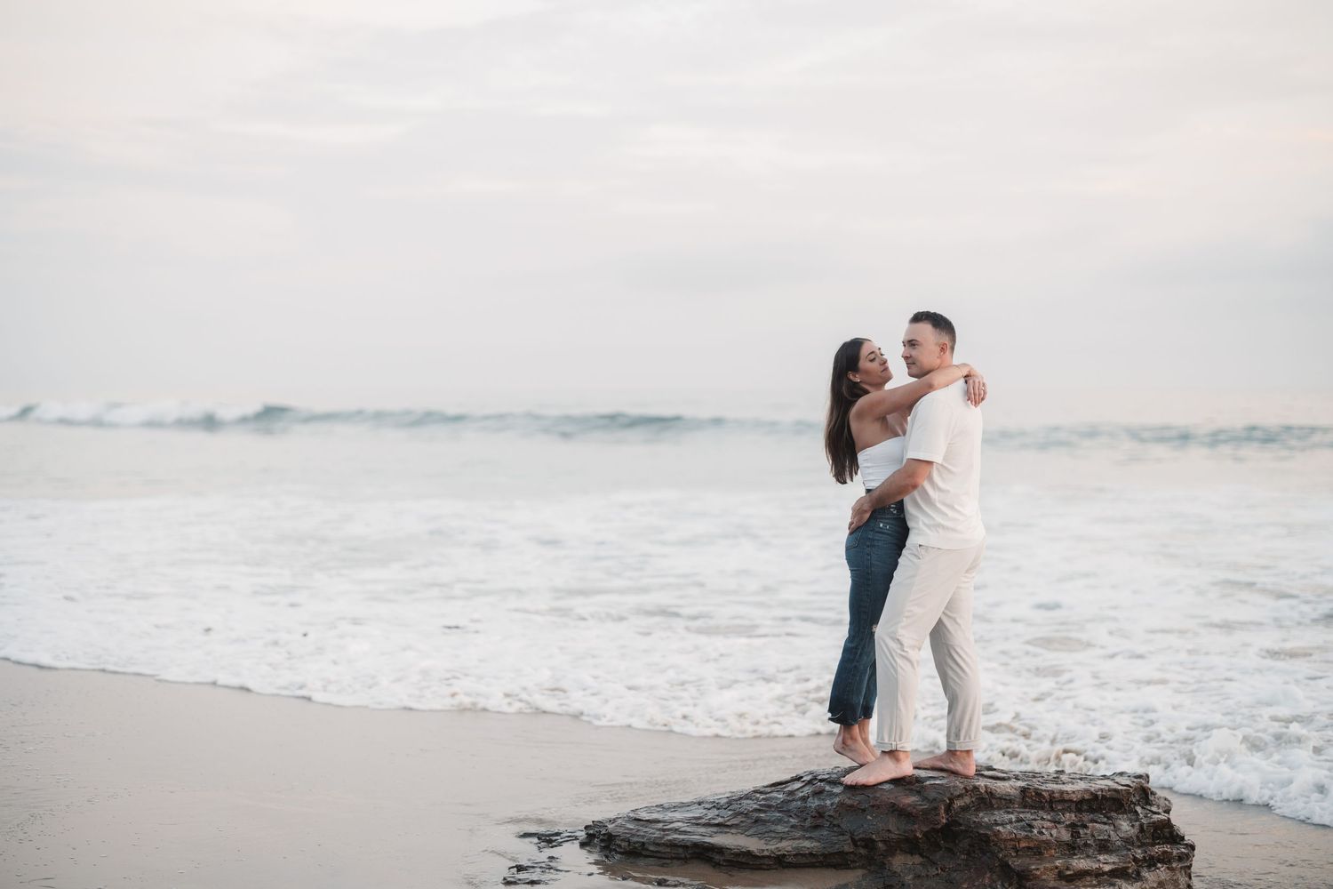 Engagement Session of a Couple at Crystal Cove in Newport Beach, California. Couple standing on a rock by the ocean.