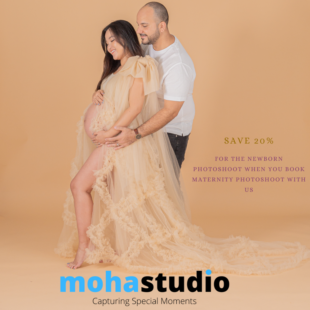 Studio maternity photo with flowing beige dress against warm backdrop.