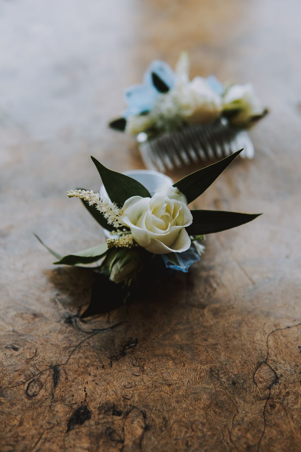 White rose and greenery boutonniere rests on a rustic wooden surface.