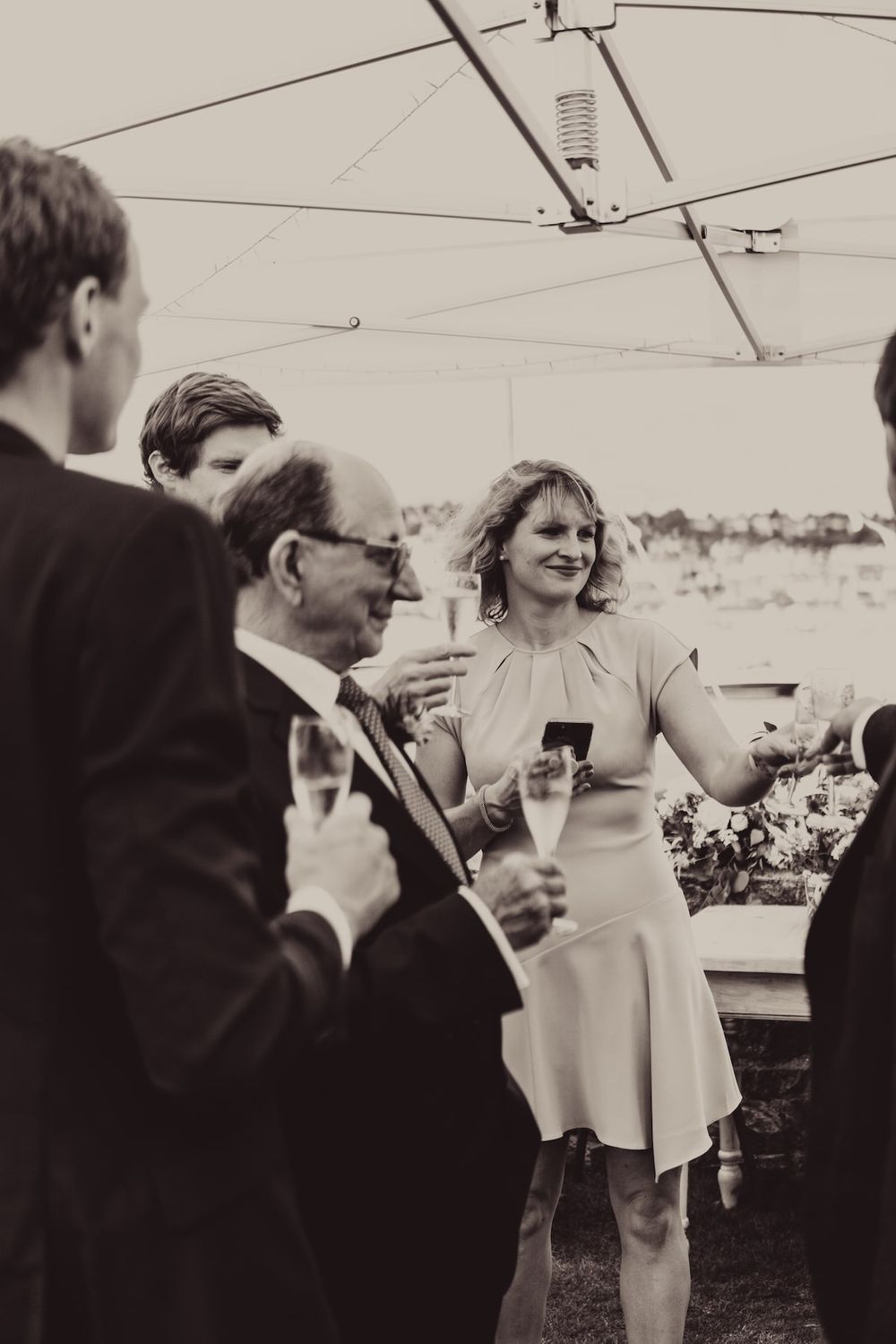 Vintage black and white photo of guests socializing at an outdoor gathering under a tent.