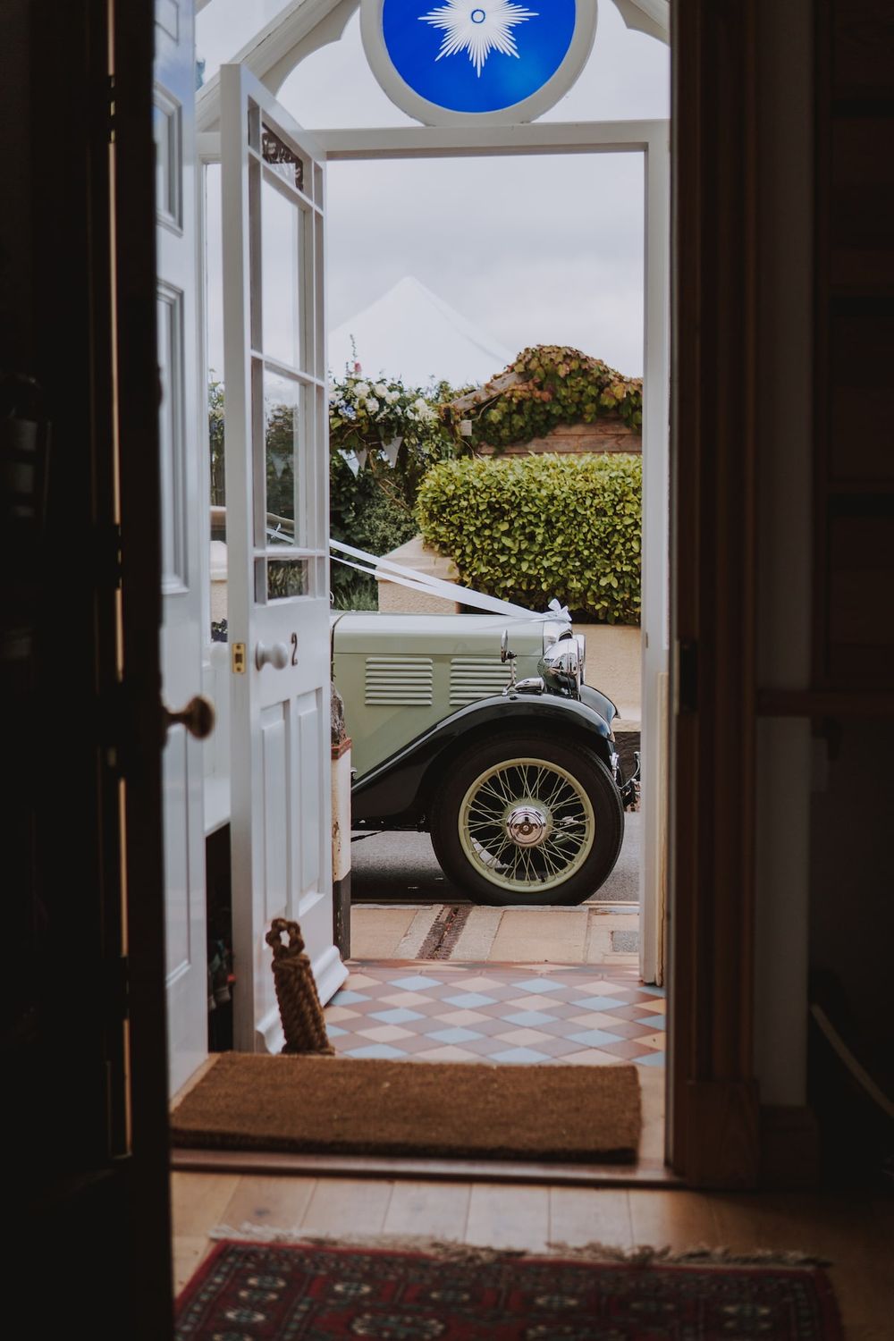 View through a doorway with blue stained glass showing a vintage car parked outside.