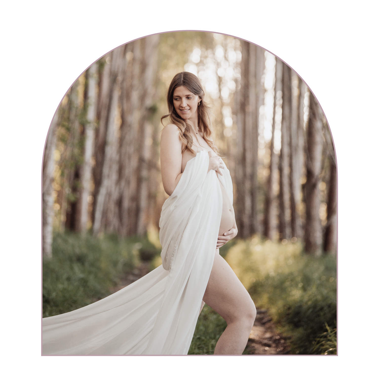 Ethereal maternity portrait in a white flowing dress among tall forest trees.