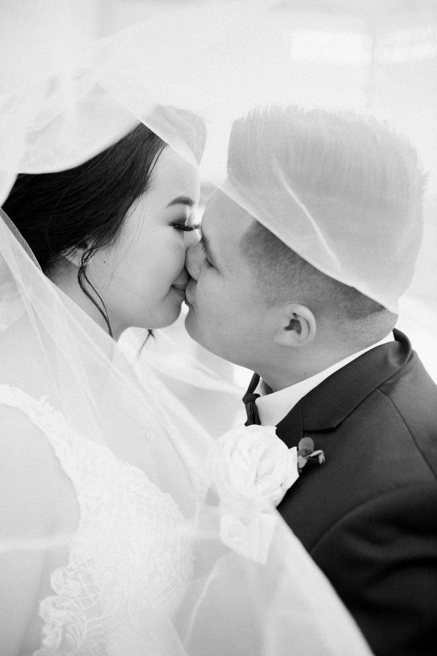 Bride and groom kiss under the veil in black and white