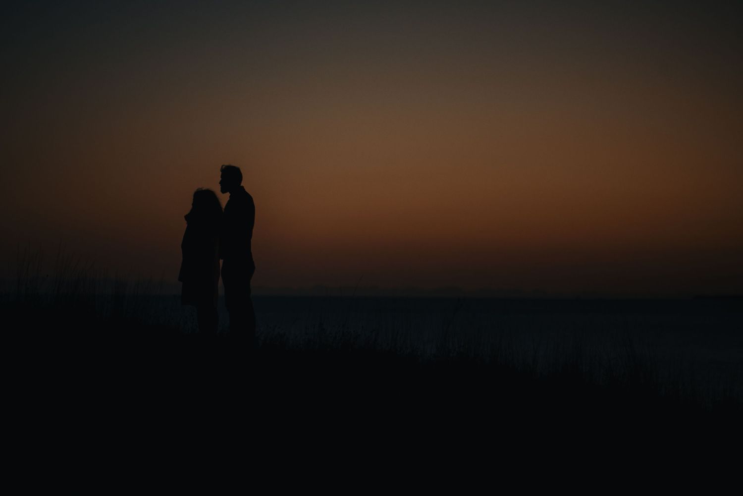 Silhouetted couple standing together against dramatic sunset sky.