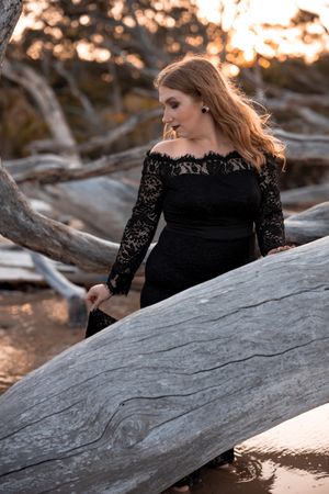 Woman in black lace dress poses on driftwood during golden hour photoshoot.