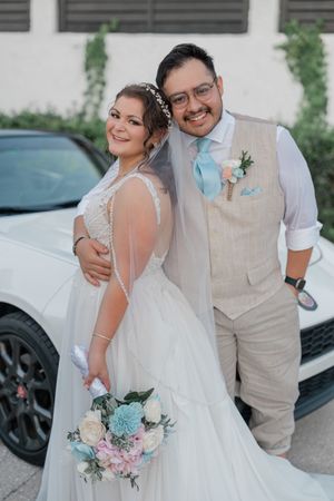A romantic wedding photoshoot featuring a couple in a white dress and tan vest with a blue and pink bouquet.