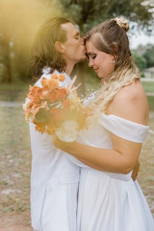 Intimate maternity portraits of couple in white dresses against warm sunlit background.