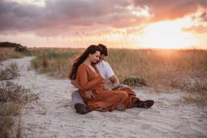 Romantic sunset photoshoot with couple embracing on sandy beach terrain.