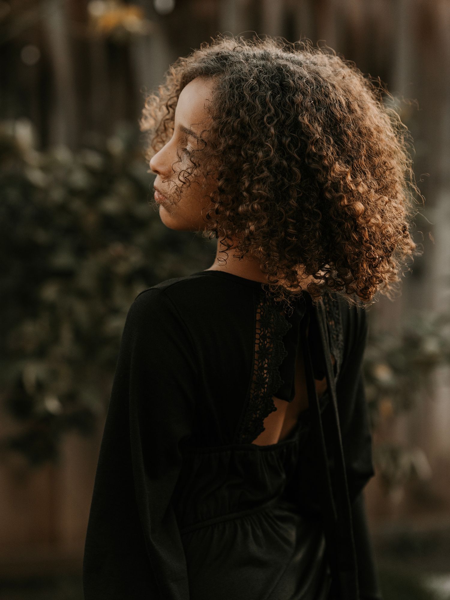 Moody side profile portrait with curly hair against warm wooden tones.