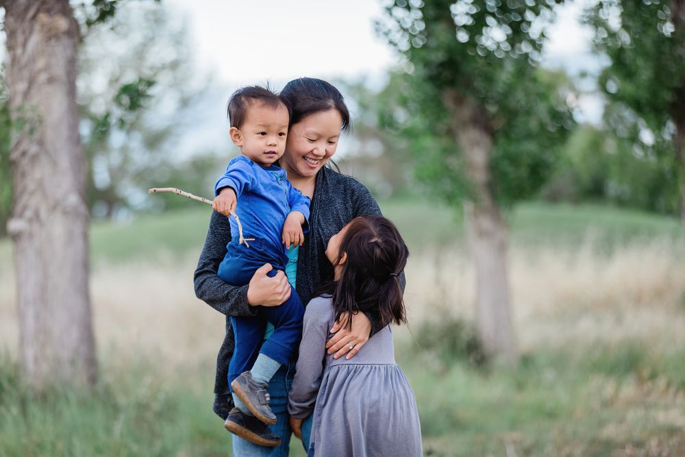 A loving family moment captured outdoors in a natural setting with tall grass and trees.
