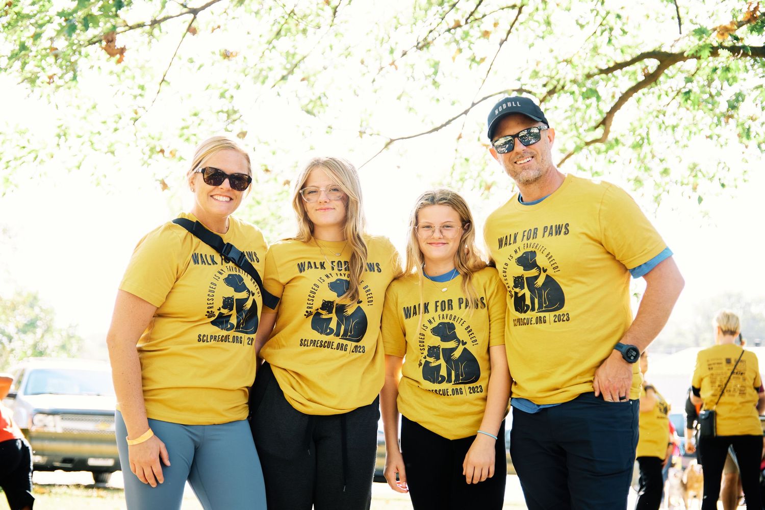 Team in bright yellow shirts gathered outdoors for a group photo under green trees.