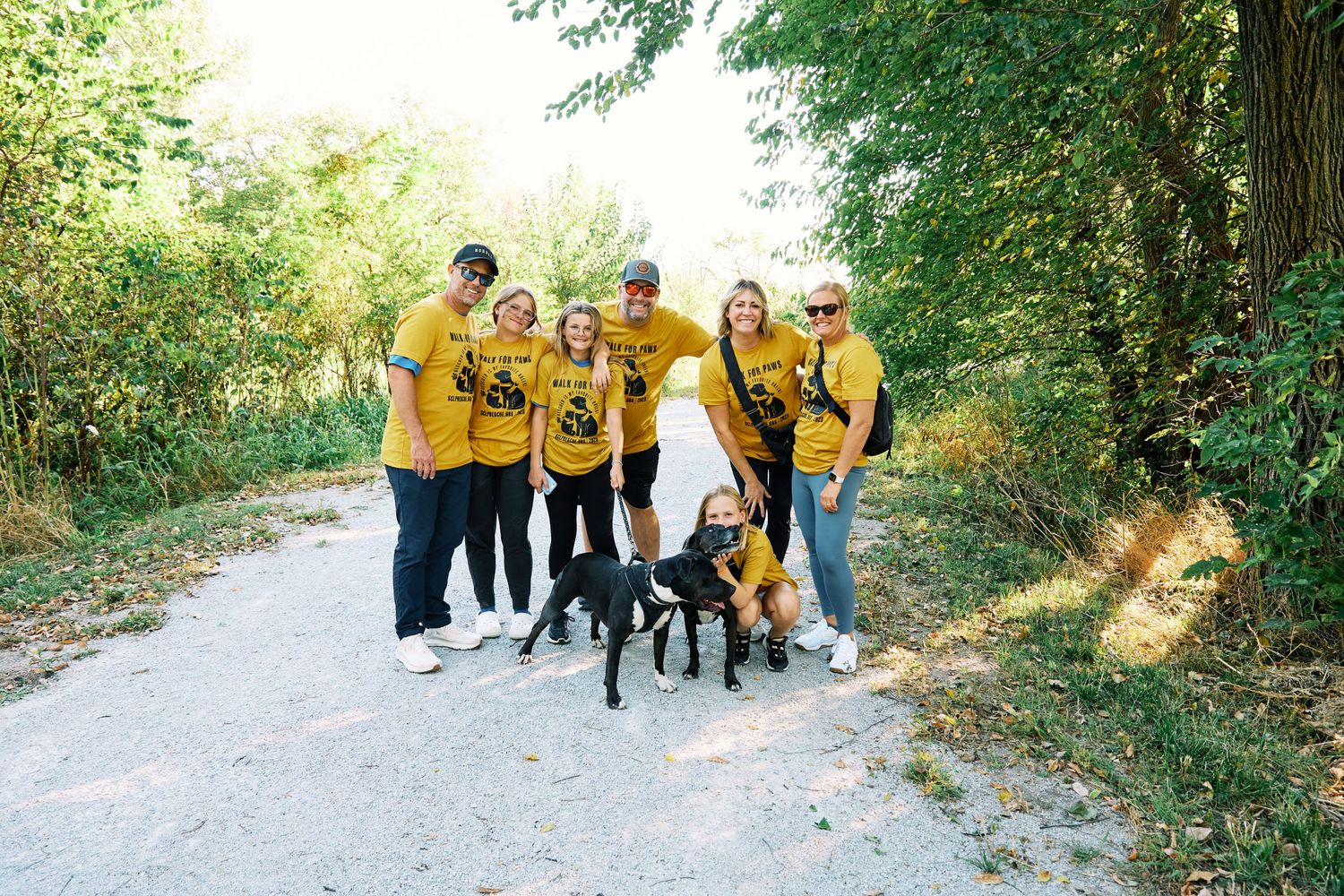 Group photo session outdoors with multiple people and pets against natural background.