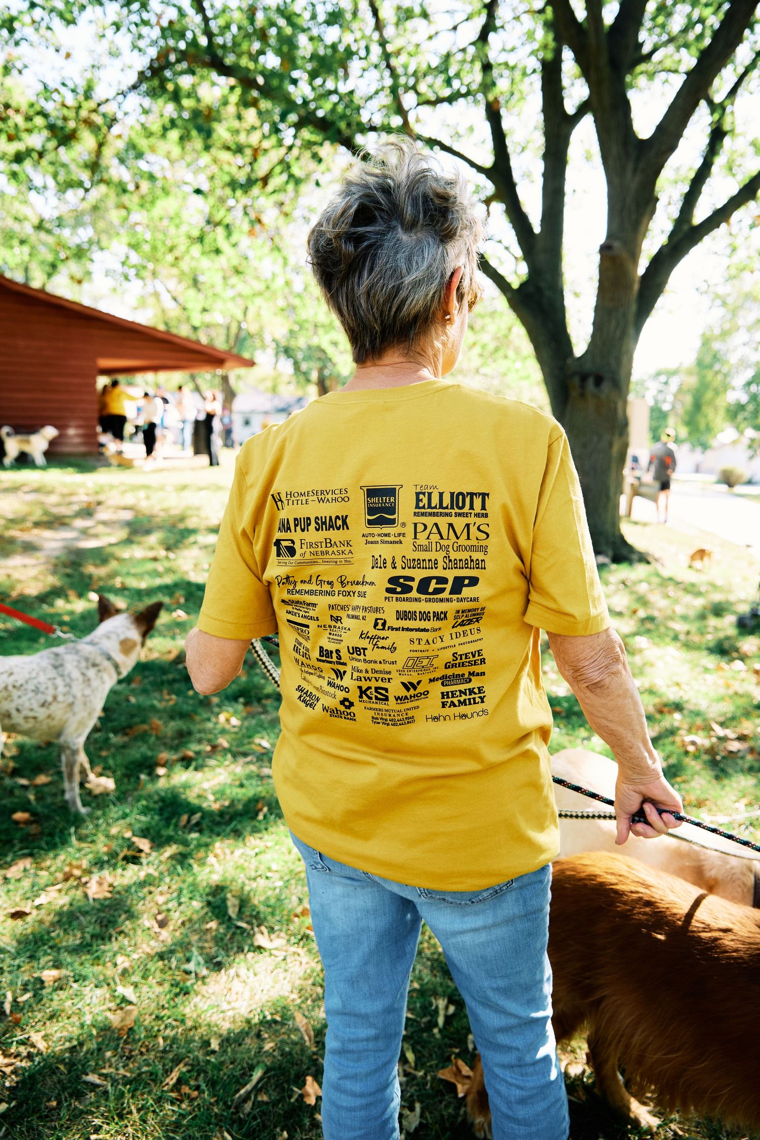 Person in yellow t-shirt and jeans standing near trees outdoors.