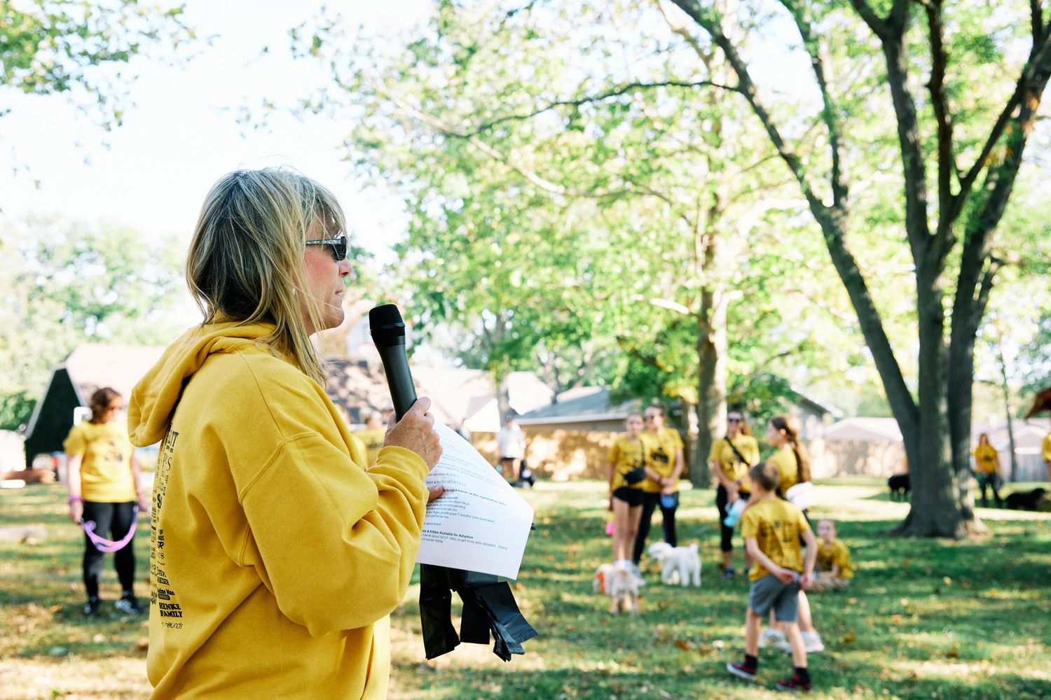 Person in yellow speaks into microphone at outdoor community event.