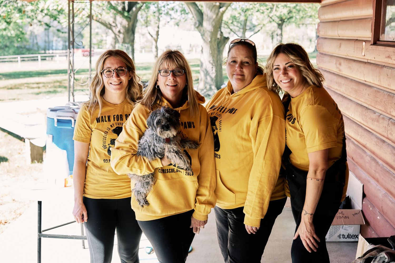 Group wearing matching yellow shirts posing together outside wooden building.