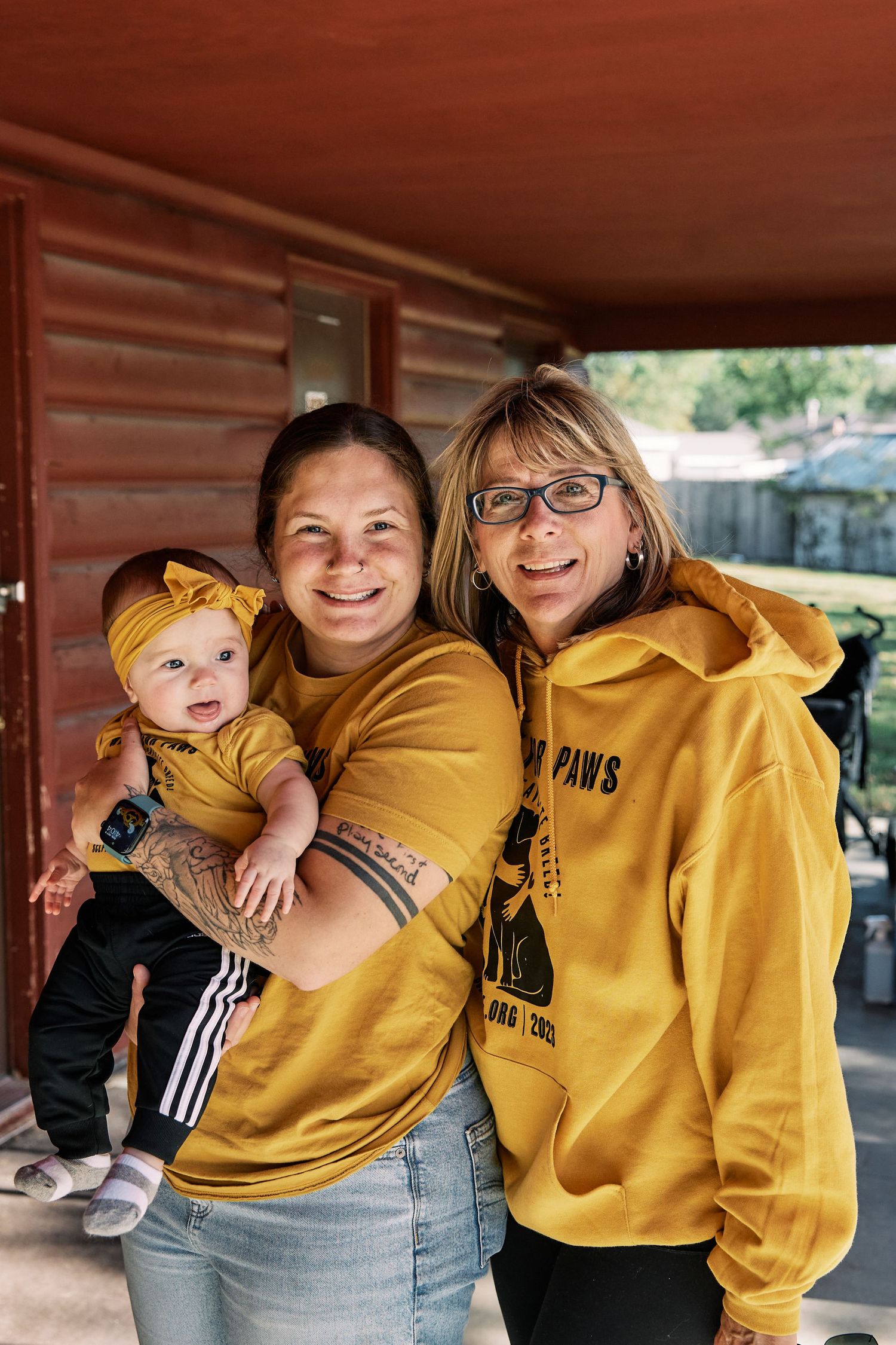 Family group wearing coordinating yellow sweatshirts posing against rustic red wall.