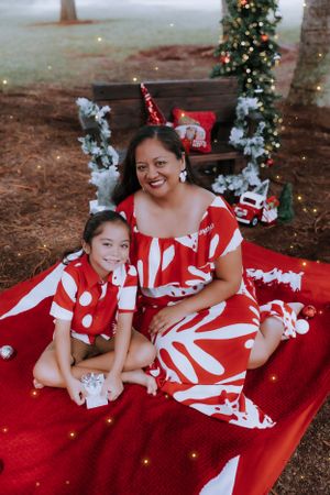 Holiday portrait on red blanket with Christmas decorations and trees in outdoor setting.
