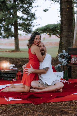 Romantic holiday couple photos on red blanket surrounded by pine trees.