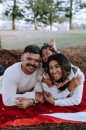 Family members cuddle close together on a red blanket outdoors during a holiday photoshoot.