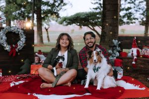 A couple sits with their dogs on a red blanket during an outdoor Christmas photoshoot.