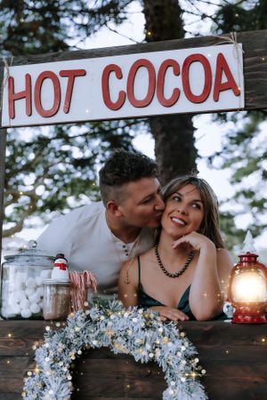 A couple shares an intimate moment at a rustic hot cocoa stand decorated for Christmas.